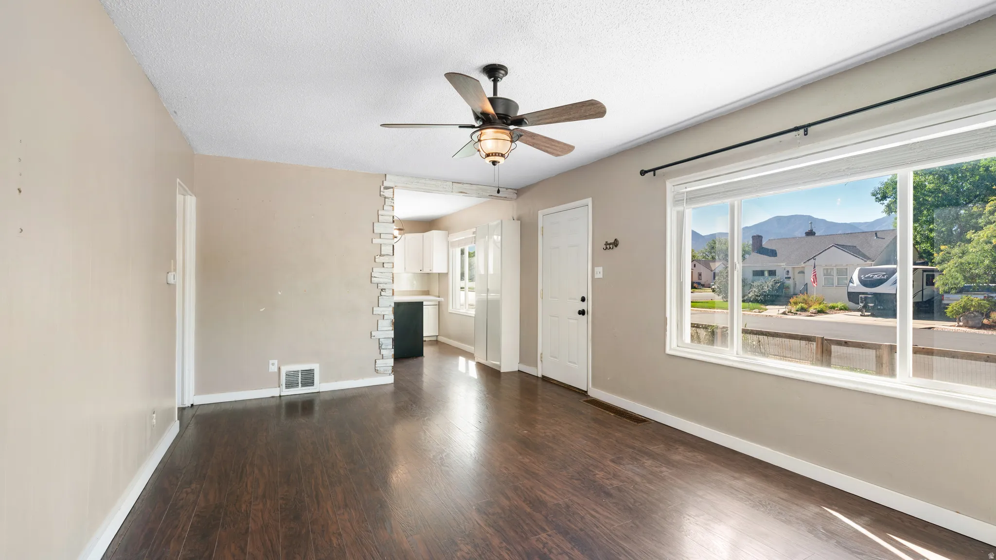 Hardwood-finish flooring, ceiling fan, and large picture window with a mountain backdrop