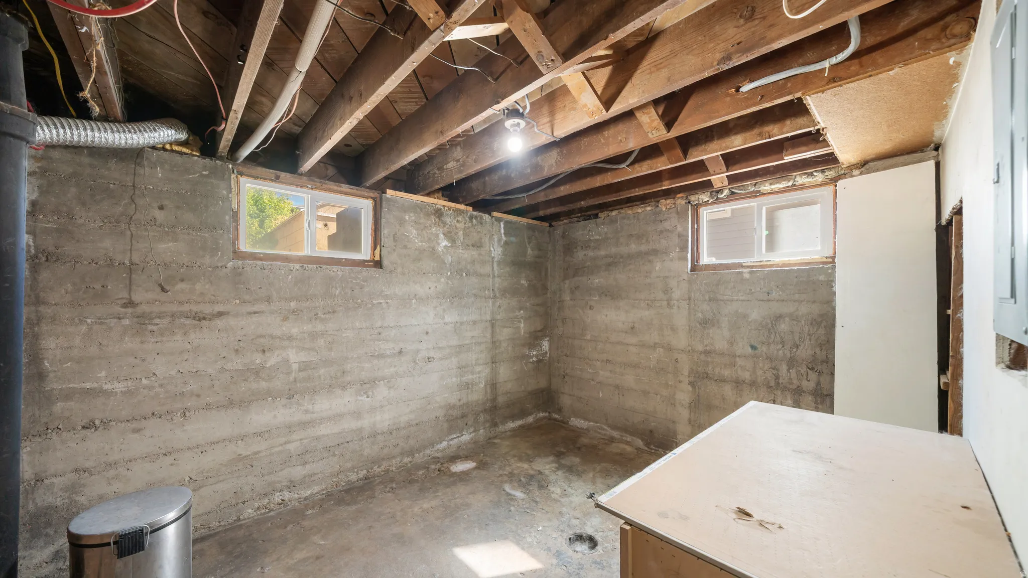 Exposed wooden ceiling joists, concrete walls, and two visible windows
