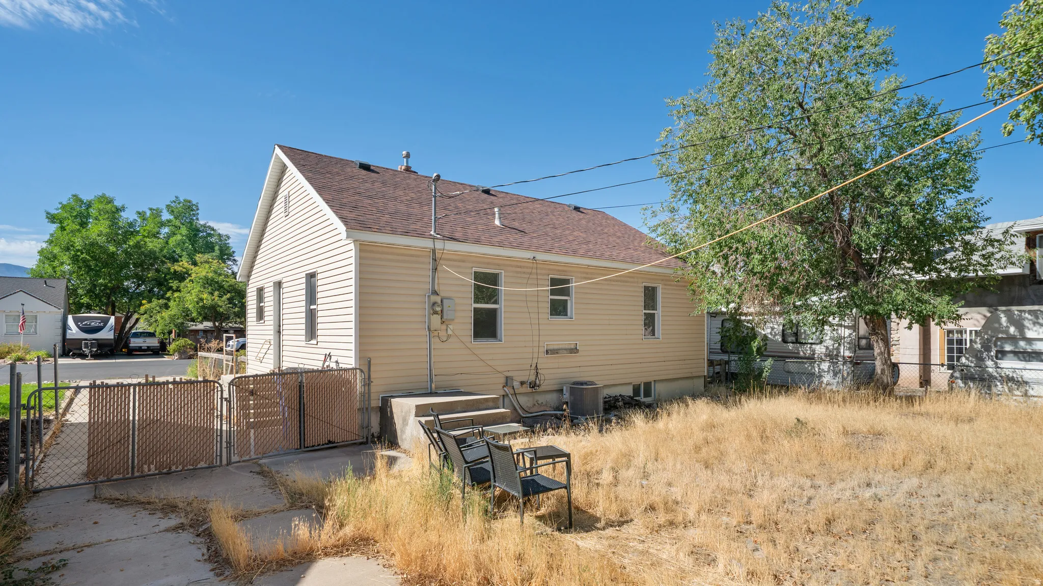 Exterior featuring light-colored siding, a brown shingled roof, a paved patio, and a chain-link fence with privacy screening
