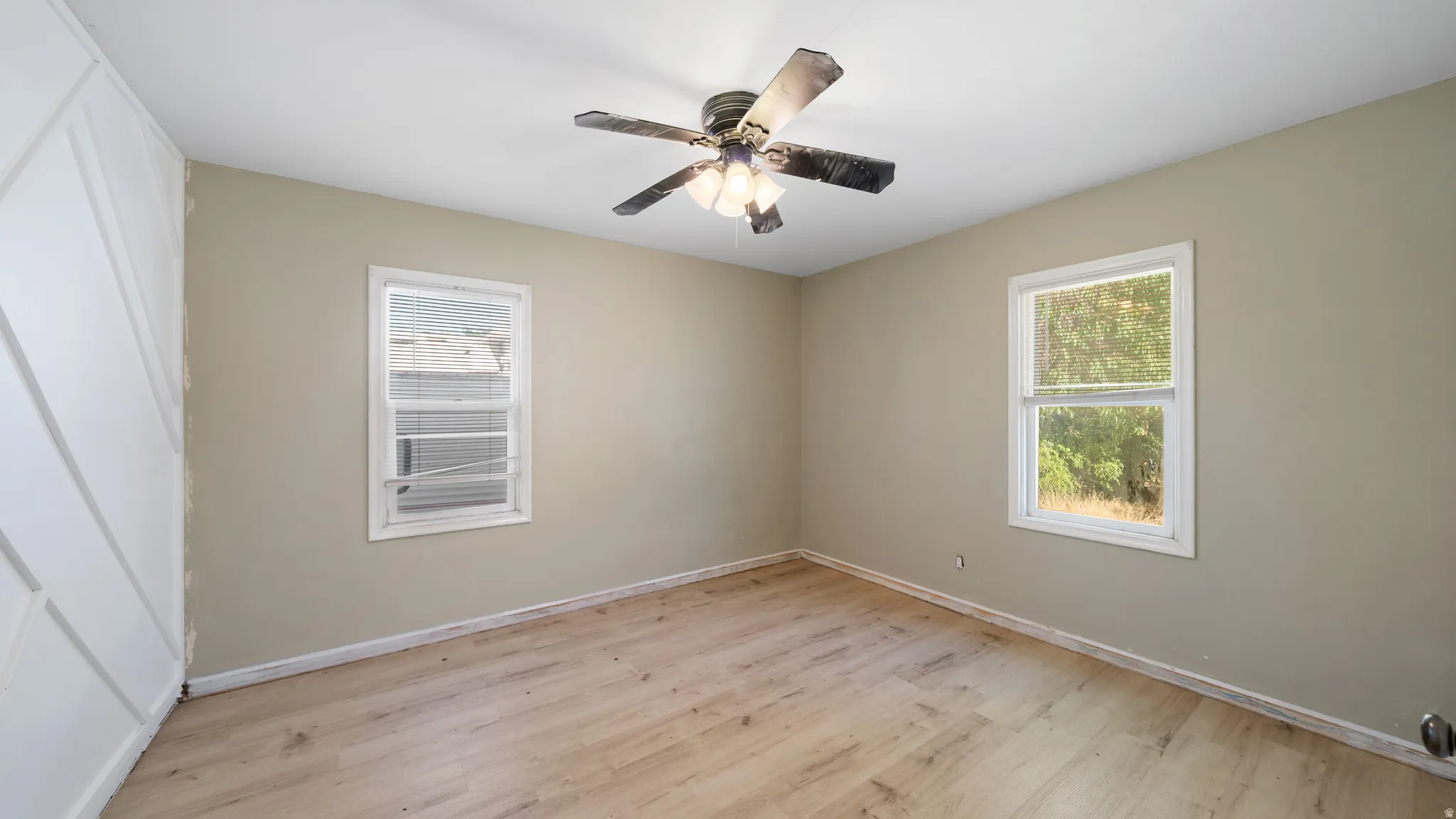Wood-finish flooring, two windows, textured accent wall, ceiling fan, and neutral paint