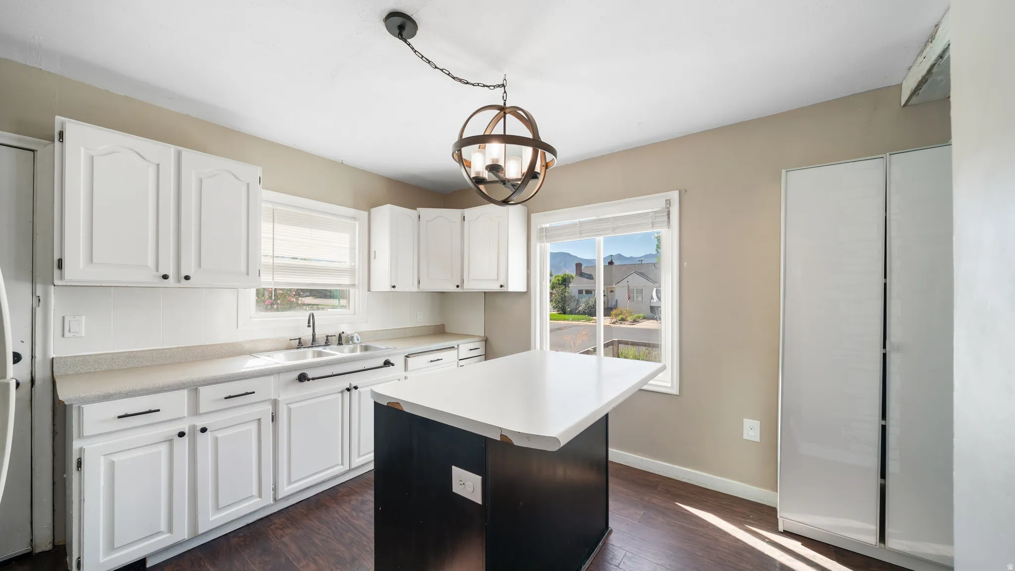 White cabinetry with black hardware, wood-finish flooring, and a central kitchen island with a white countertop