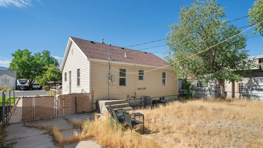 Exterior featuring light-colored siding, a brown shingled roof, a paved patio, and a chain-link fence with privacy screening