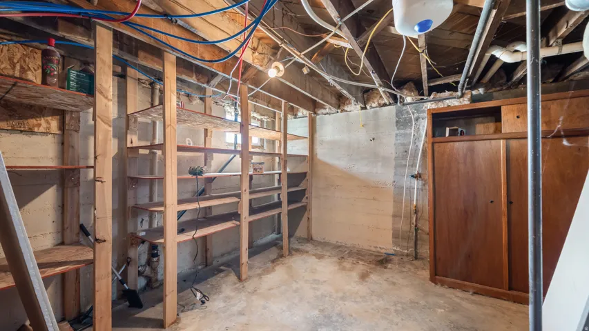 Unfinished basement space featuring exposed wood joists, concrete walls, built-in wooden shelving, and a built-in wooden cabinet