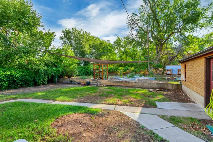 Expansive backyard featuring a concrete patio, established garden beds, shade structure, and mature trees