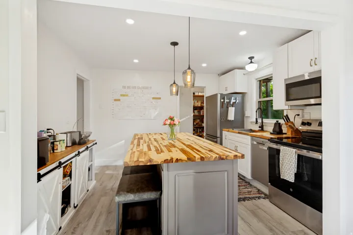 Kitchen featuring white cabinetry, stainless steel appliances, wood-finish countertops, an island with a wood-block surface, and pendant lighting