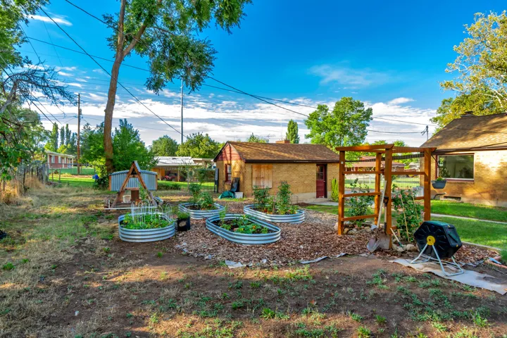 Backyard featuring multiple raised garden beds, a wood-finish trellis, an outbuilding with a shingled roof, and a mature tree