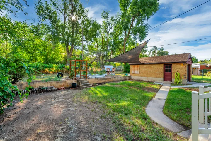 Expansive backyard featuring a detached brick building, concrete pathway, and mature trees