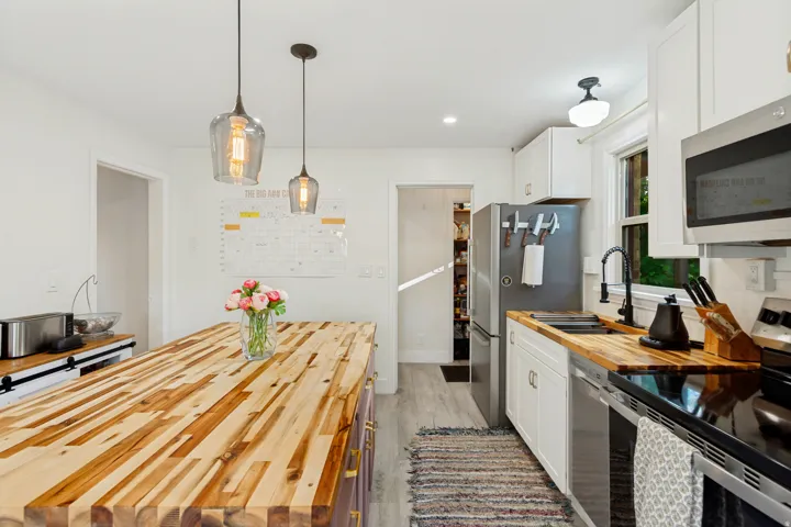 Kitchen featuring a wood-finish island, two pendant light fixtures, white cabinetry, wood-finish countertops, and stainless steel appliances