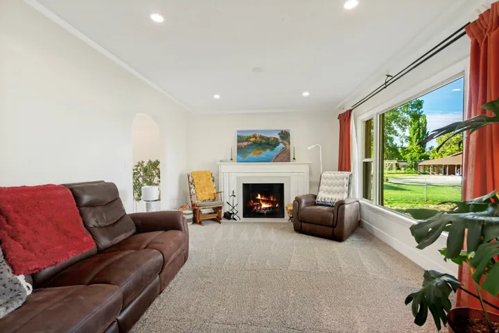 Recessed lighting, arched doorway, large picture window, fireplace with mantel, and light-toned carpeting