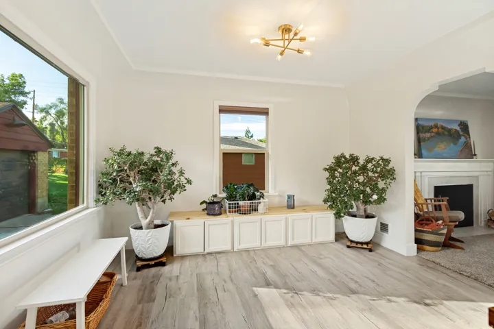 Light wood-finish flooring, built-in cabinetry with a wood countertop, large window, arched doorway, and a modern ceiling light fixture