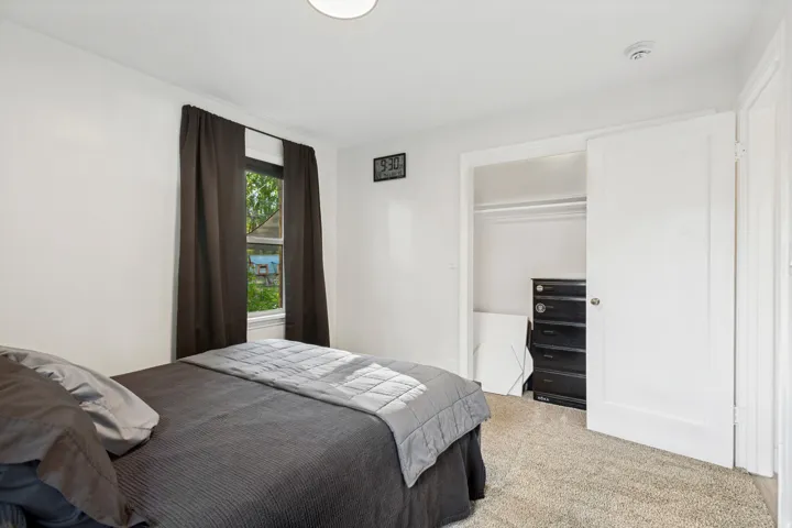 White walls, light-colored carpet, window with dark curtains, and a built-in closet with white bi-fold doors