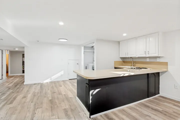 Kitchenette featuring white upper cabinetry, black lower cabinetry, a stainless steel sink, and wood-finish flooring