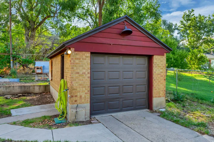 Detached brick-clad garage with a dark panel garage door and a red siding gable