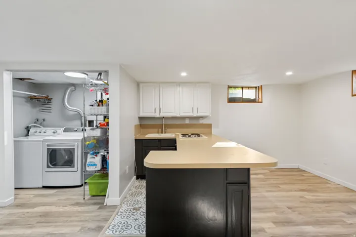 Kitchenette with white upper cabinetry and dark base cabinetry, built-in cooktop, and an undermount sink