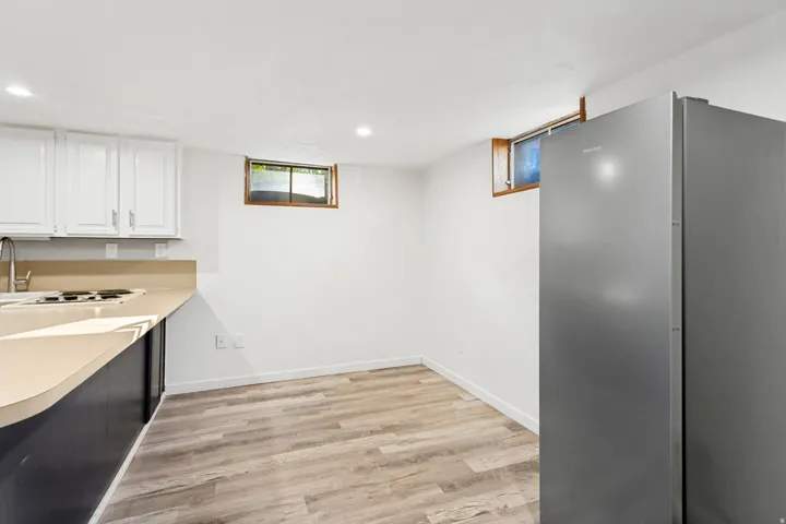 White cabinetry, light countertop, wood-finish flooring, recessed lighting, and a stainless steel refrigerator