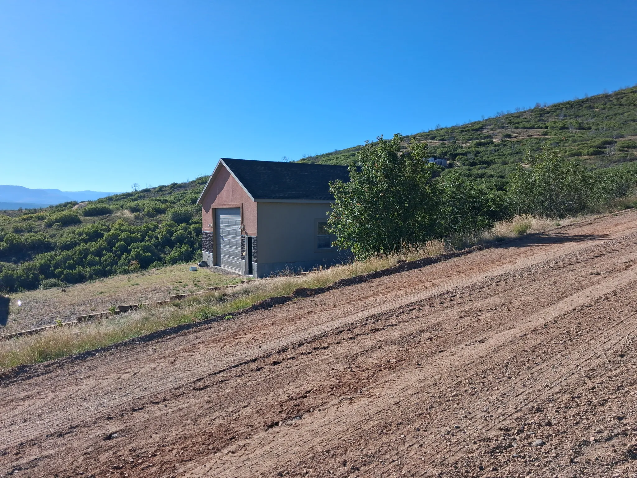 Sloping terrain with an accessory structure featuring a dark roof, brown siding, and stone accents