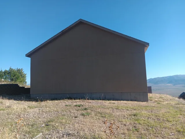 Stucco exterior with a pitched roof, featuring exposed eaves and a concrete foundation