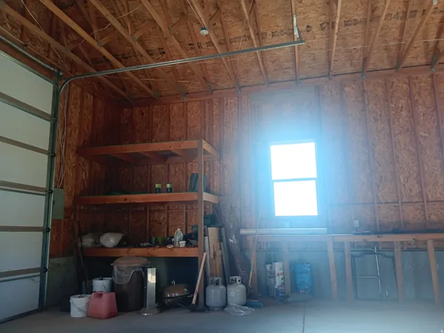 Garage space featuring exposed wood framing, a large window, a garage door, and built-in wood shelving