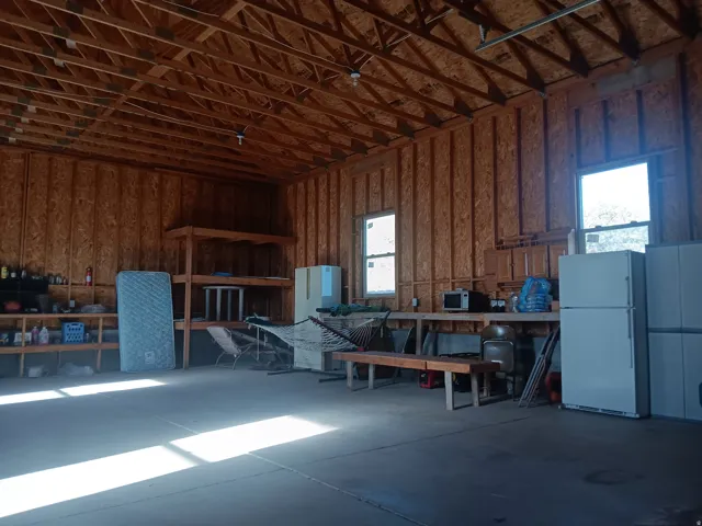 Spacious interior featuring exposed wooden rafters, multiple windows, a concrete floor, and built-in shelving