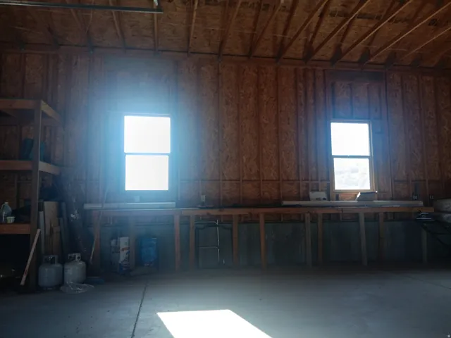 Unfinished garage with exposed wood framing, two windows, and an integrated workbench