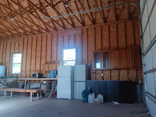 Spacious garage with exposed wood ceiling trusses, two windows, wall-mounted cabinetry, and a concrete floor