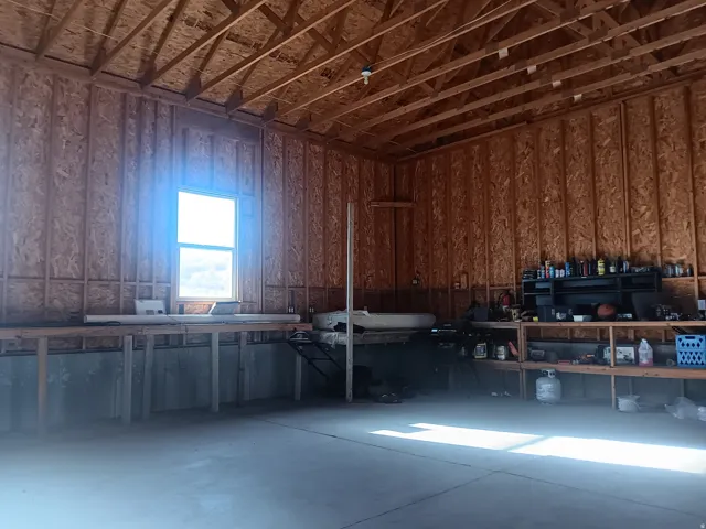 Spacious interior featuring exposed wood ceiling trusses, oriented strand board walls, a concrete floor, and a large window