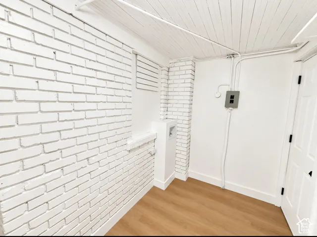 White-painted brick wall, wood-finish flooring, white paneled door, and exposed conduit