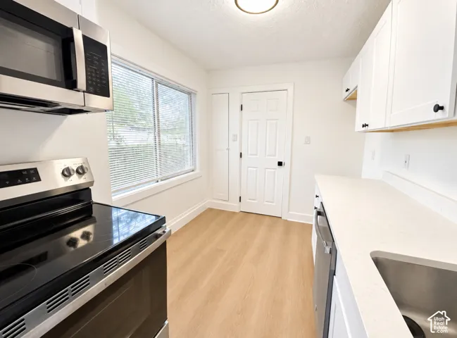Kitchen featuring stainless steel appliances, white cabinetry, light countertops, a stainless steel sink, and wood-finish flooring