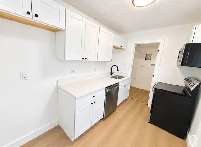 White cabinetry with black hardware, light-toned countertops, stainless steel dishwasher, black range, and wood-finish flooring