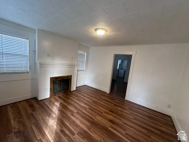 White-painted brick fireplace with a metal insert, wood-finish flooring, white walls, and a ceiling-mounted light fixture