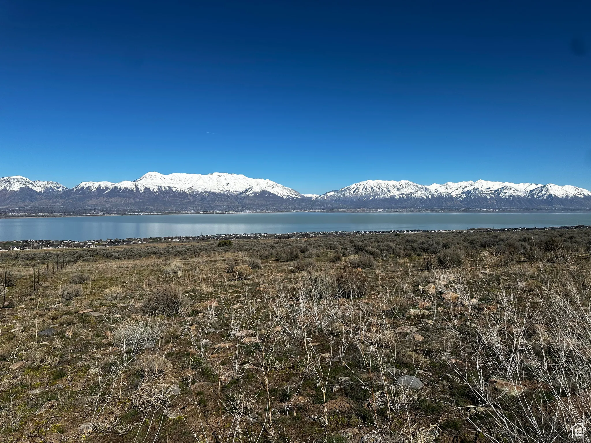 Expansive natural landscape featuring distant snow-capped mountains, a large body of water, and broad clear skies