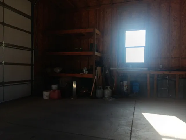 Garage featuring concrete flooring, exposed wood stud wall construction, a single-pane window, and built-in wood shelving units