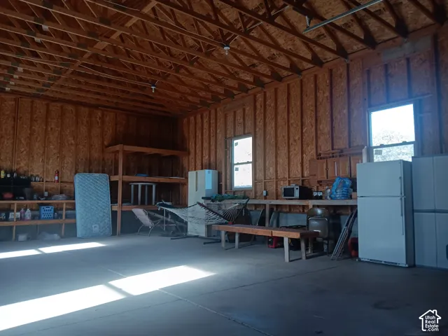 Expansive garage featuring exposed wood framing, concrete flooring, double windows, and built-in wood shelving units