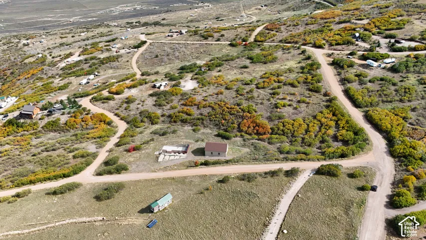 Aerial perspective of a sprawling hillside acreage featuring native vegetation, unpaved access roads, a detached structure with a shingled roof, and a prepared concrete foundation