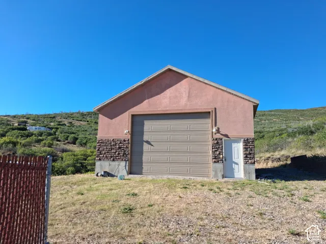 Detached garage featuring a stucco exterior with stone veneer accents, a roll-up RV-height vehicle door, a dedicated pedestrian entry, and exterior wall-mounted lighting