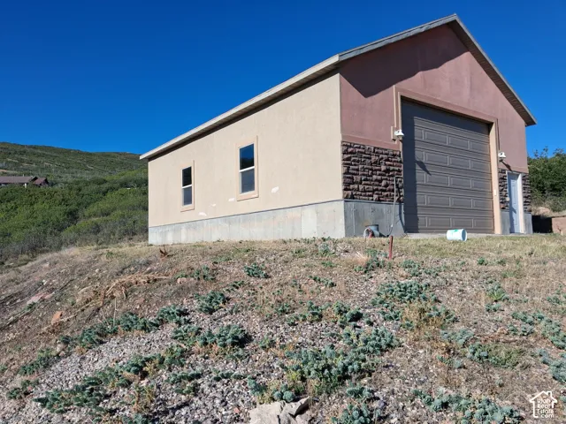 Detached structure featuring a stucco and stone exterior, concrete foundation, and roll-up garage door