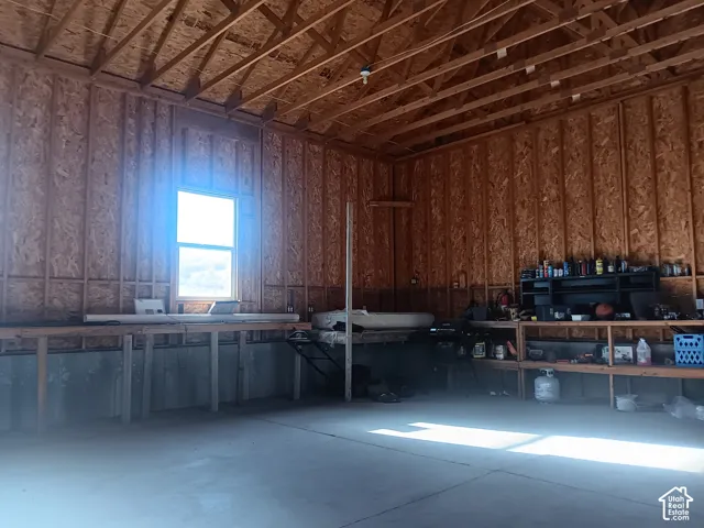 Unfinished interior space featuring exposed wood-stud wall framing, open-truss ceiling rafters, concrete flooring, and built-in wood shelving units