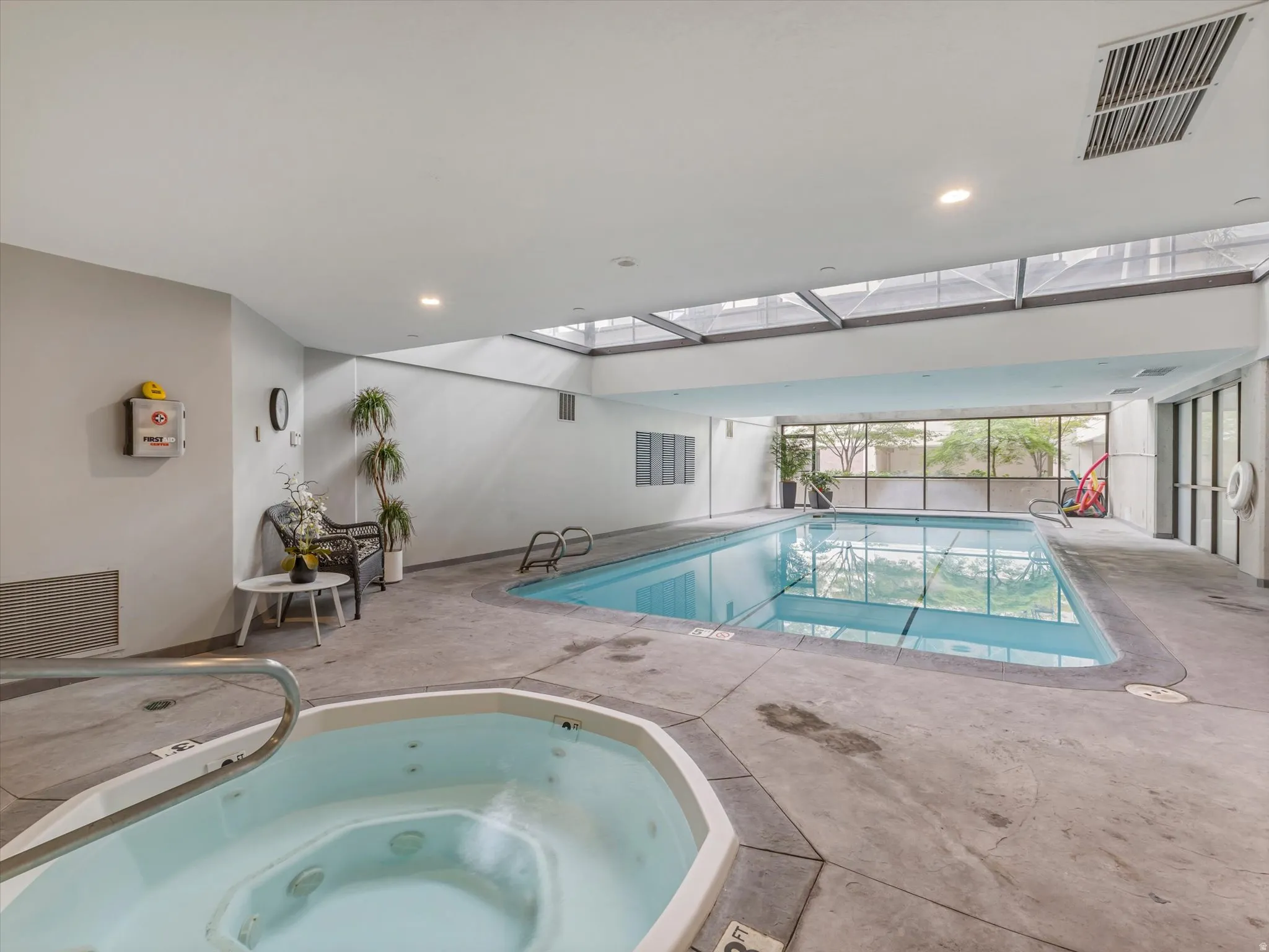 Indoor swimming pool, integrated hot tub, concrete surround, skylight ceiling, and full-height exterior windows