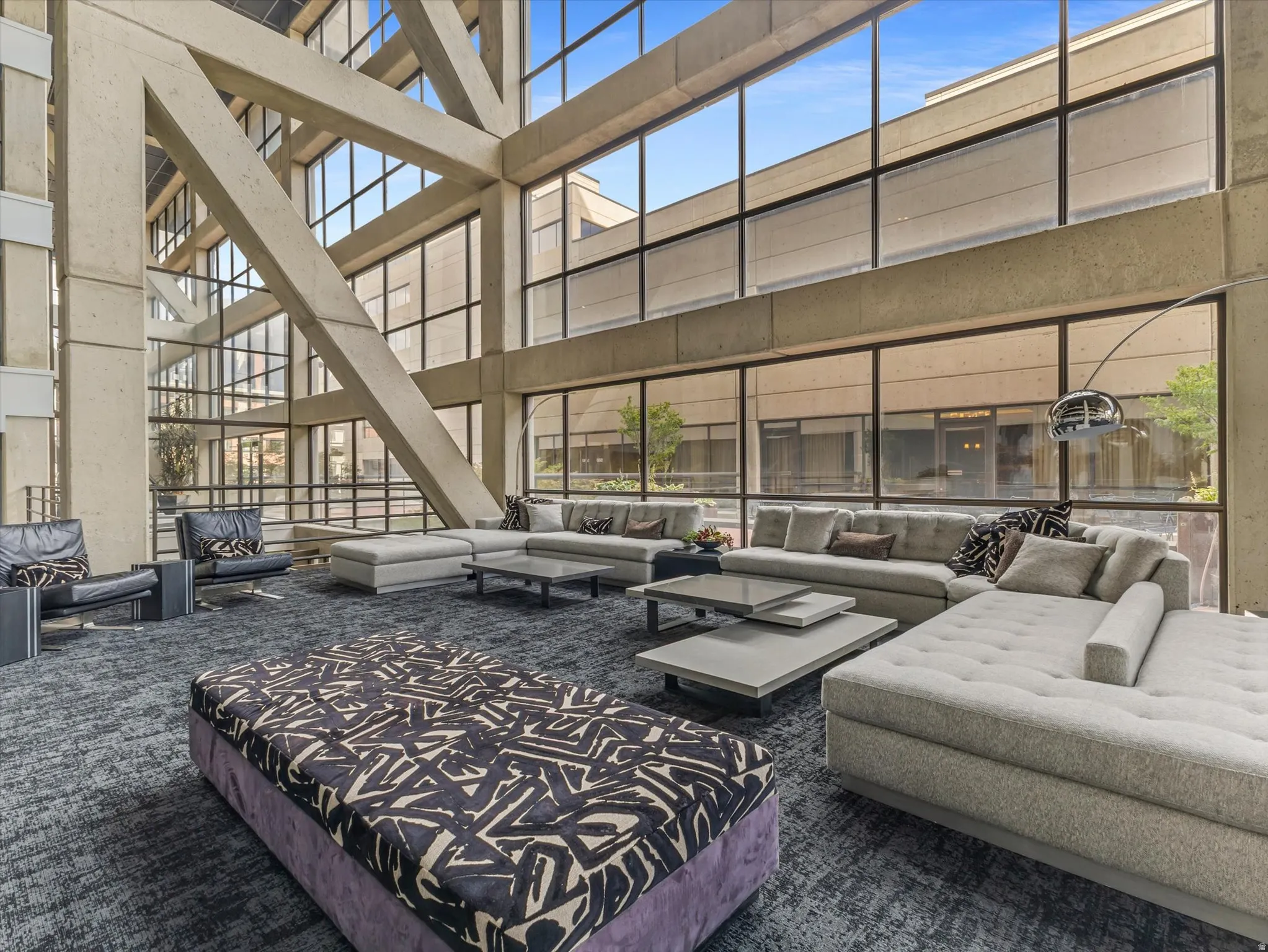 Expansive common area featuring a high-ceiling atrium with structural beams, full-height window walls, and upholstered seating