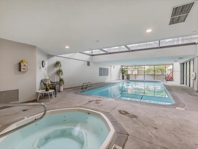 Indoor swimming pool, integrated hot tub, concrete surround, skylight ceiling, and full-height exterior windows