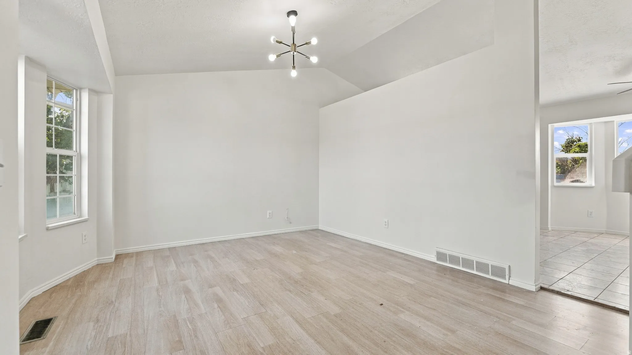 Vaulted ceilings, a contemporary light fixture, wood-finish flooring, and a bay window