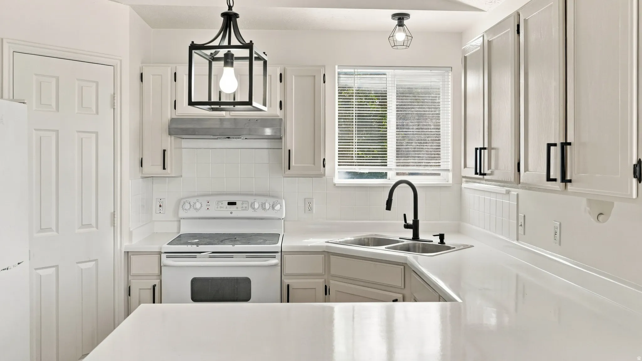 Kitchen with white cabinetry, stainless steel double basin sink, solid surface countertops, and a full tile backsplash