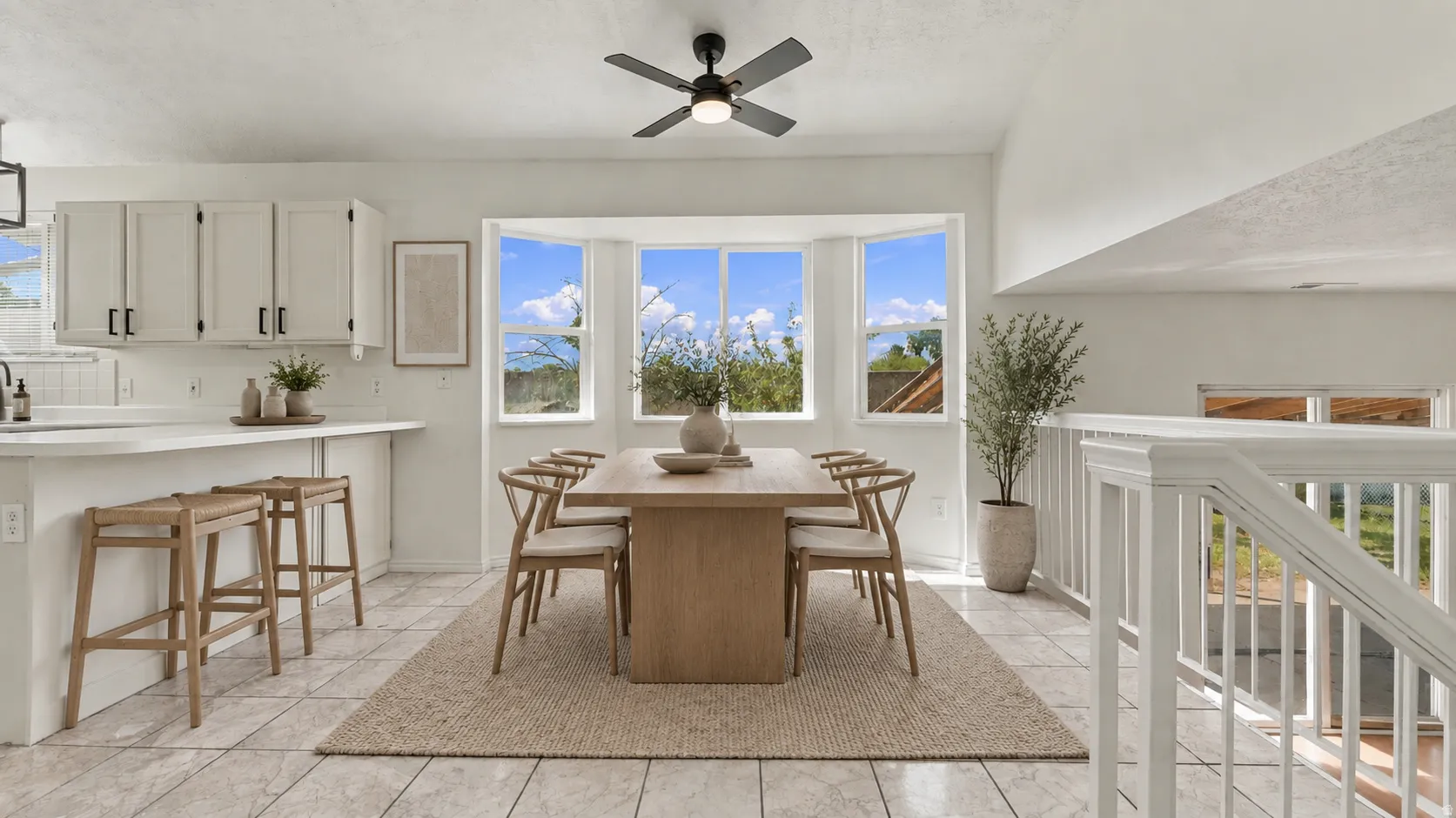 Integrated kitchen and dining area featuring a breakfast bar with seating, white cabinetry, a bay window, a ceiling fan, and tiled flooring