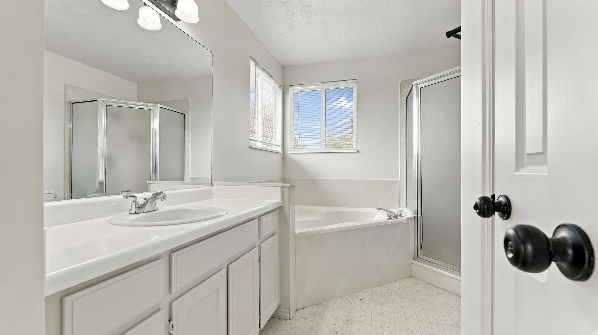 Double-door entry to bath featuring a vanity with integrated sink, built-in bathtub, and a separate glass-enclosed shower