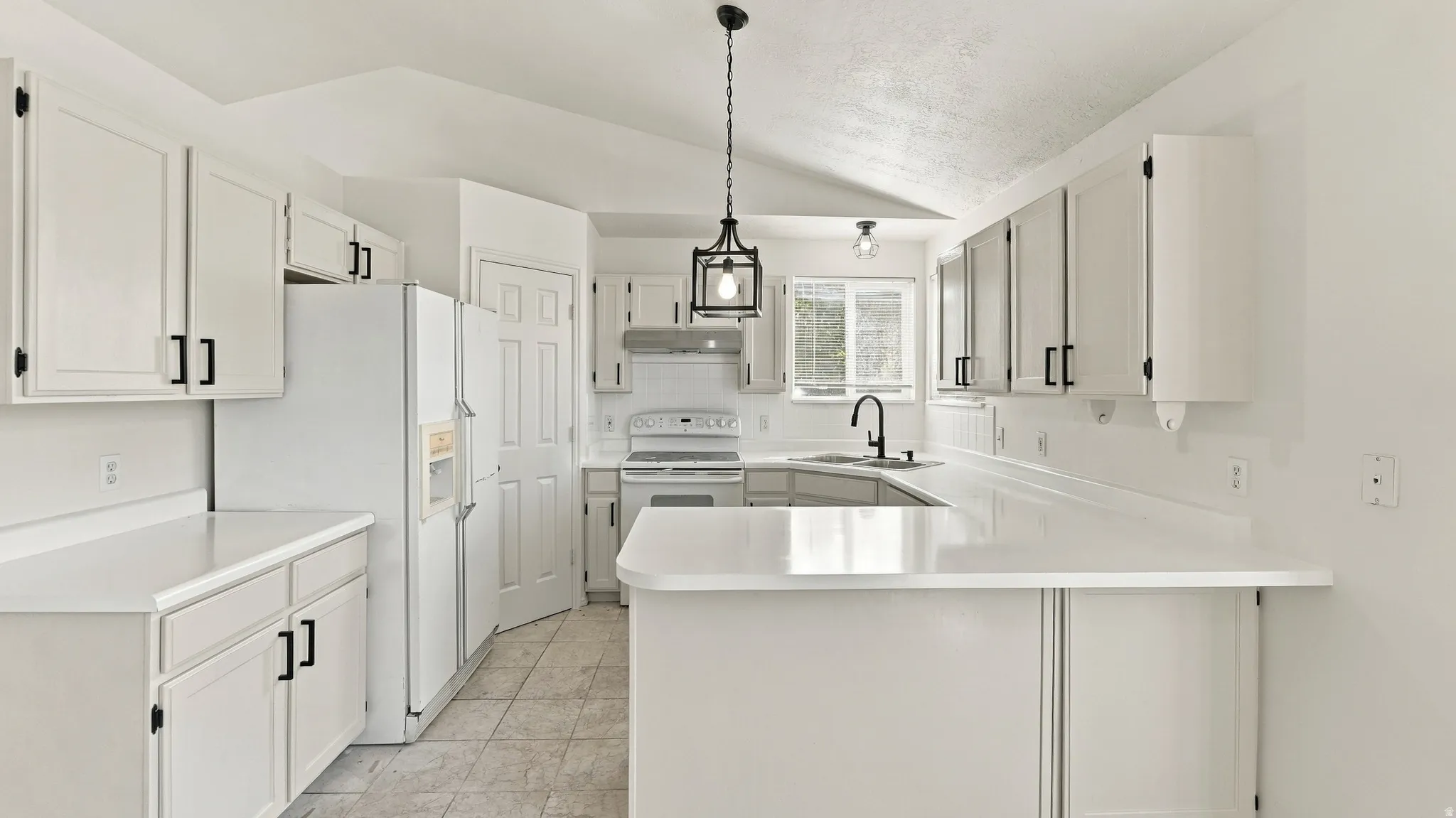 Kitchen featuring white cabinetry with black hardware, U-shaped countertops, ceiling-mounted light fixtures, and a vaulted ceiling