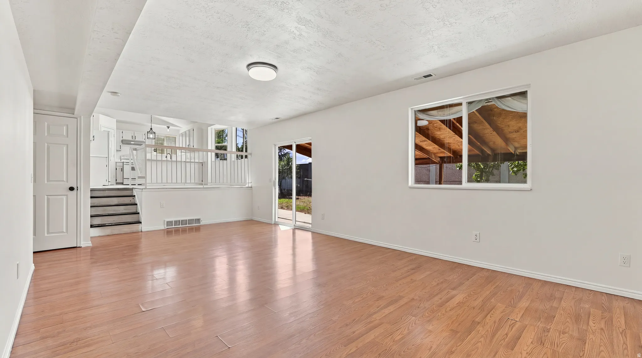 Wood-finish flooring, white walls, ceiling-mounted light fixture, sliding glass door, and a window