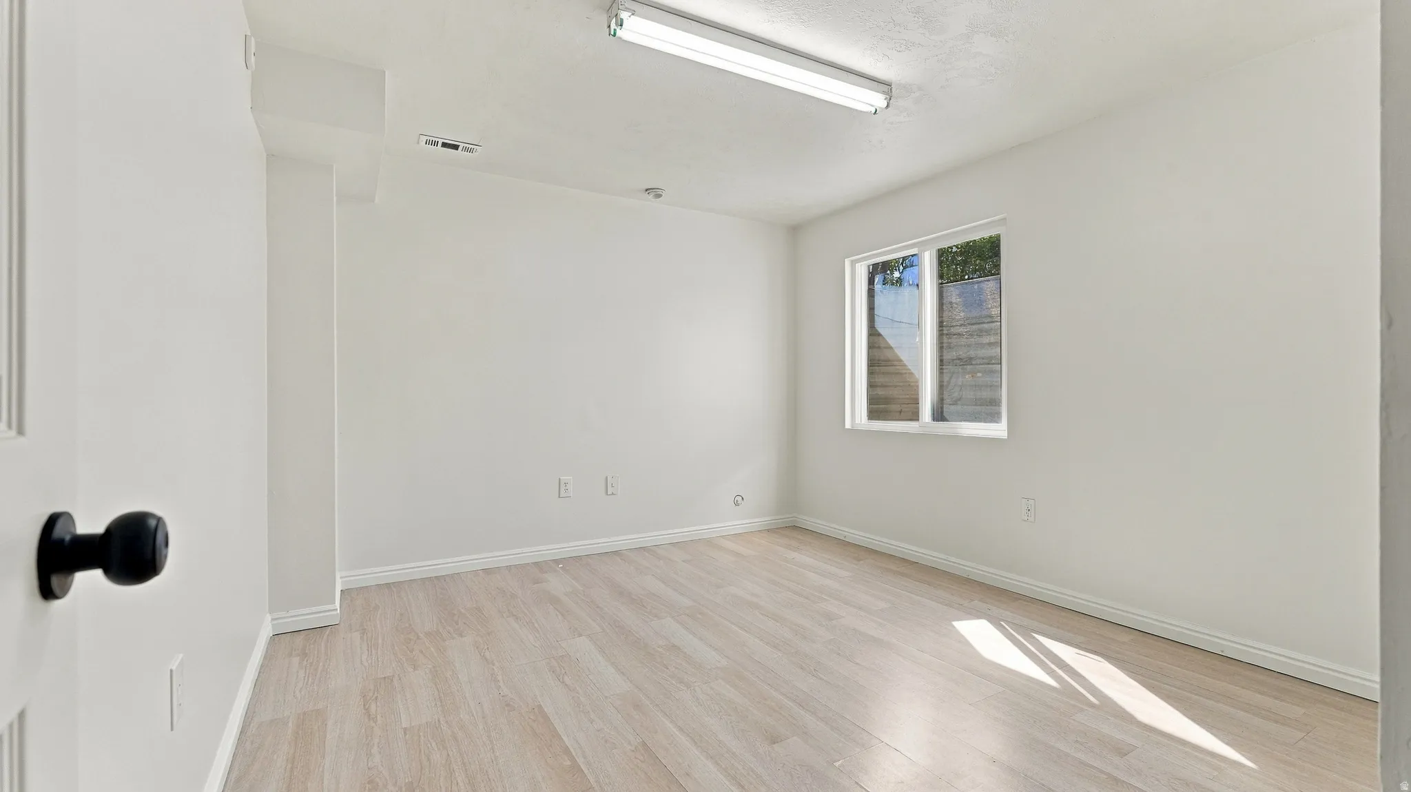 Light wood-finish flooring, white walls, and a window with a white frame