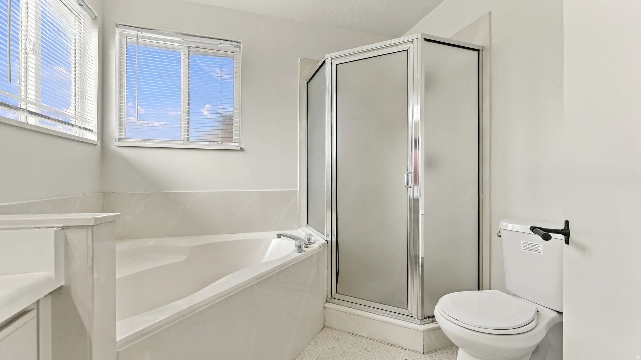 Soaking tub with tile surround, enclosed shower, and window with horizontal blinds