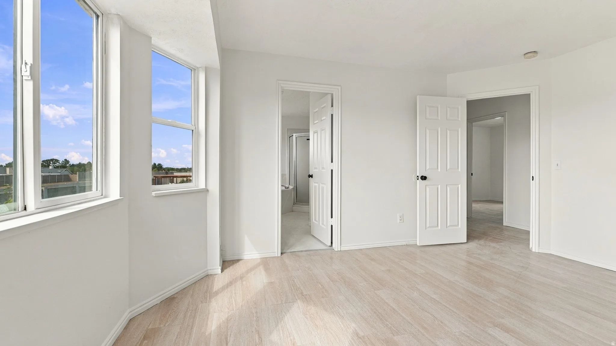 Light wood-finish flooring, white walls, multiple windows, solid panel doors with matte black hardware, and an overhead recessed light