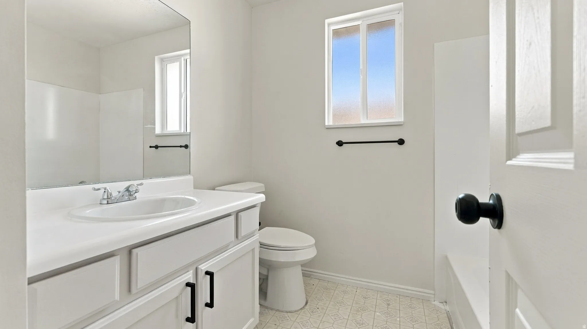 Bathroom with a white vanity, integrated sink, and black cabinet hardware